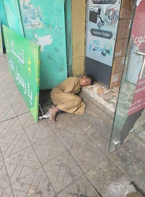 صورة تختزل المشهد المختل في صنعاء.. طفل جائع وحافي القدمين نائم على رصيف بجوار لافتة "لبّيك يا رسول الله"